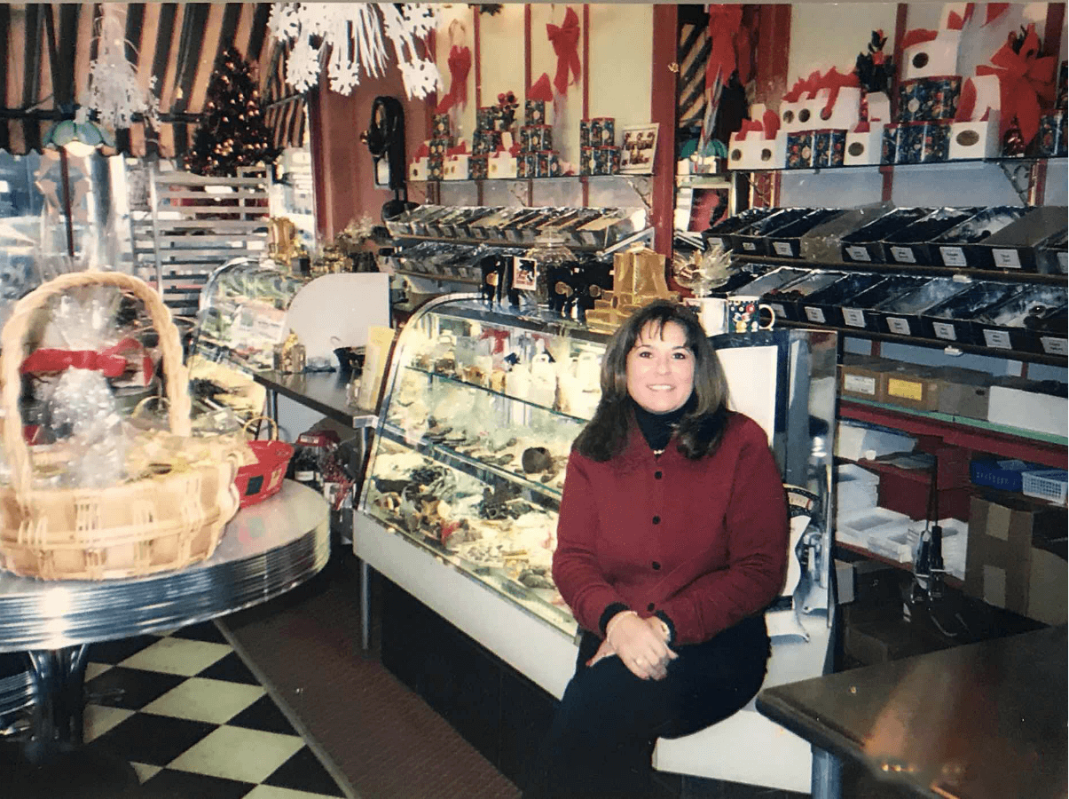 dona sitting in front of chocolate display case