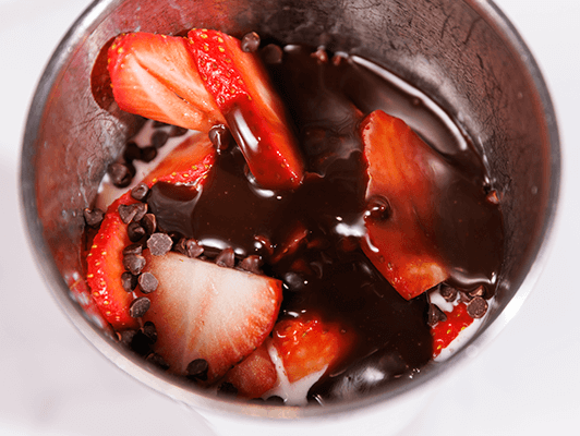 strawberries and chocolate syrup with chocolate chips in a cup